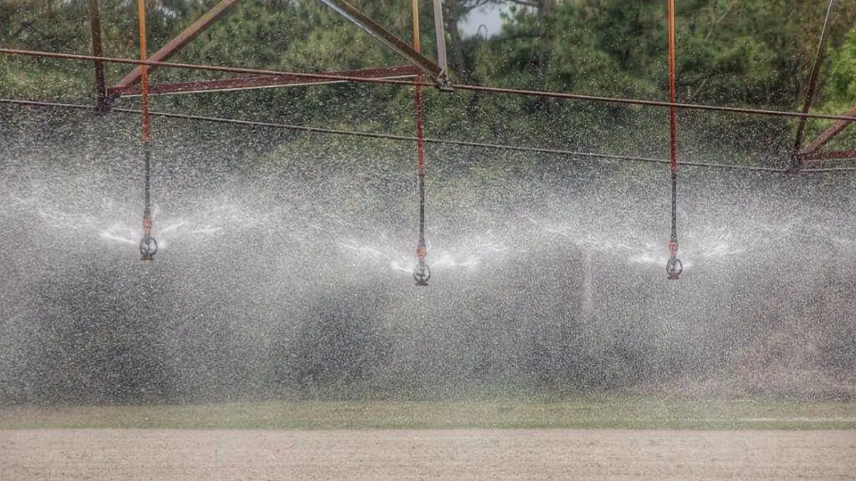 Multiple suspended sprinkler heads spraying over bare prepared soil