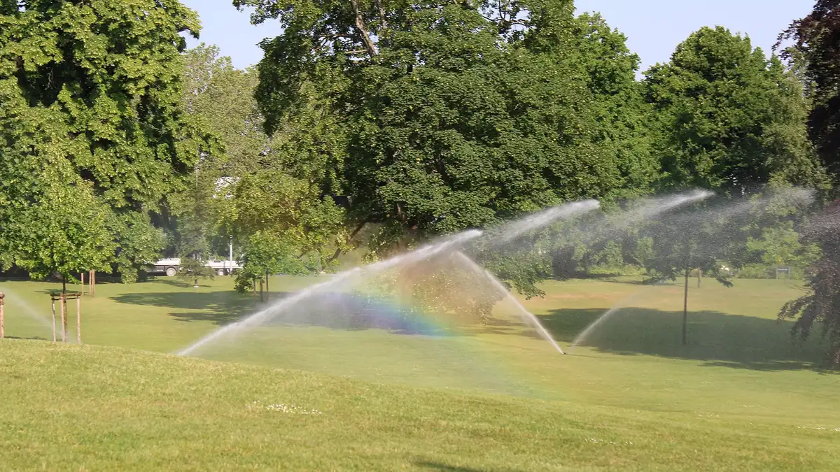 Rotor sprinkler watering a manicured lawn with rainbow mist