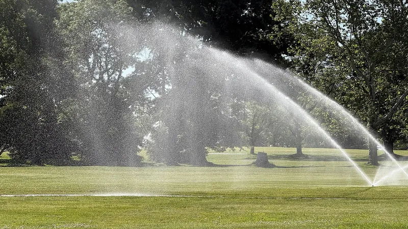 Multiple sprinkler heads spraying an arc over park turf